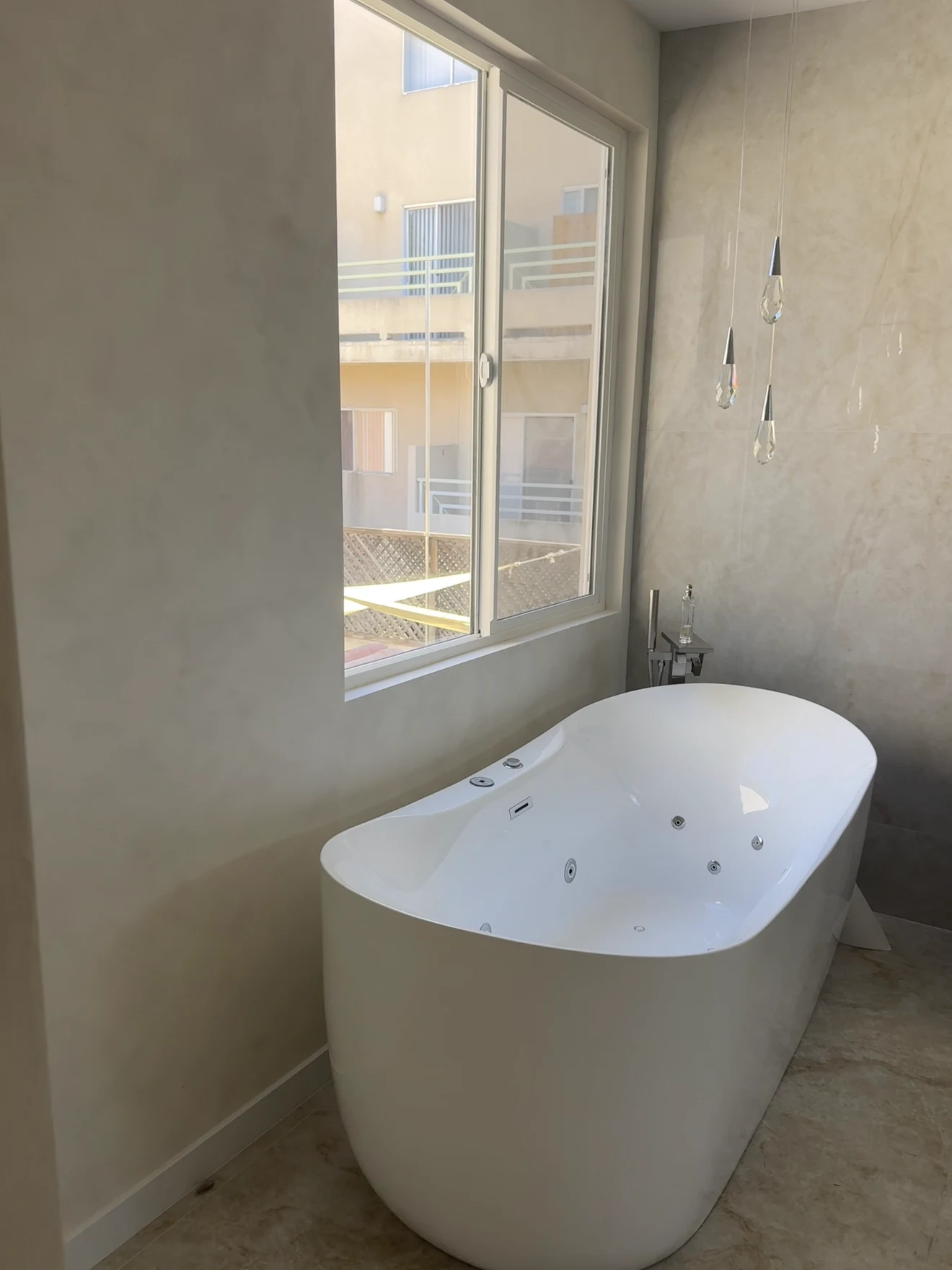 Same corner in Santa Ana after: light stone-look walls and a freestanding jetted tub under the window