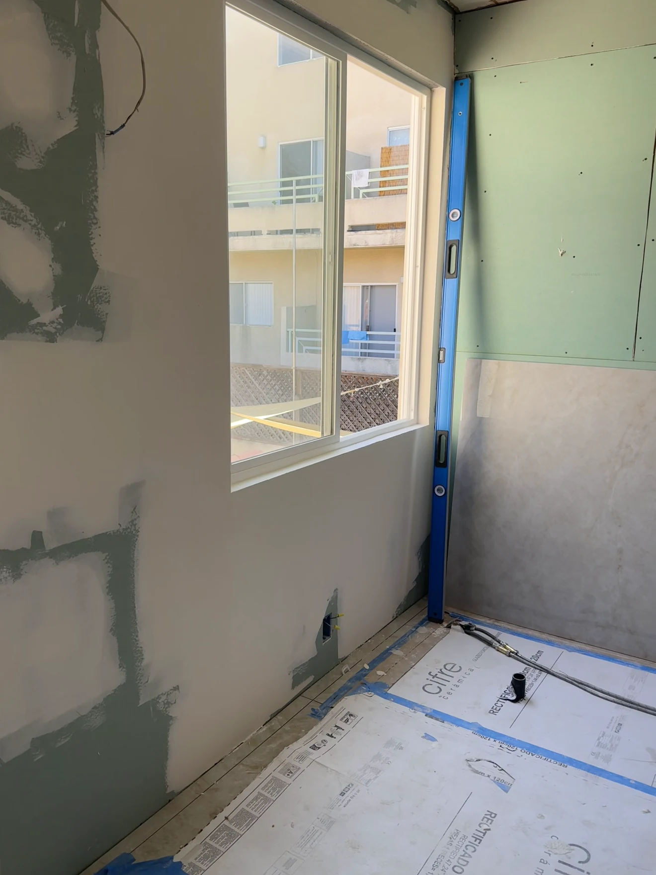 Bathroom in Santa Ana before: patched drywall around a corner window, floor covered in protective paper