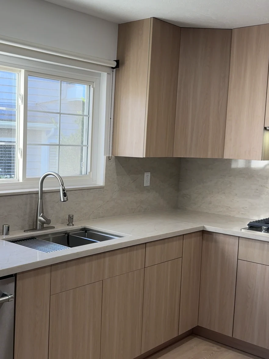Same kitchen in Tustin after: wood-grain cabinets, stone backsplash and an undermount sink under the window