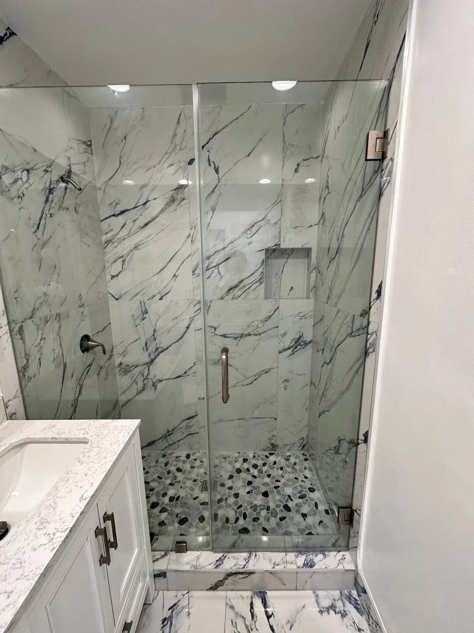 Walk-in shower with blue-veined marble-look walls and a pebble floor in Tustin