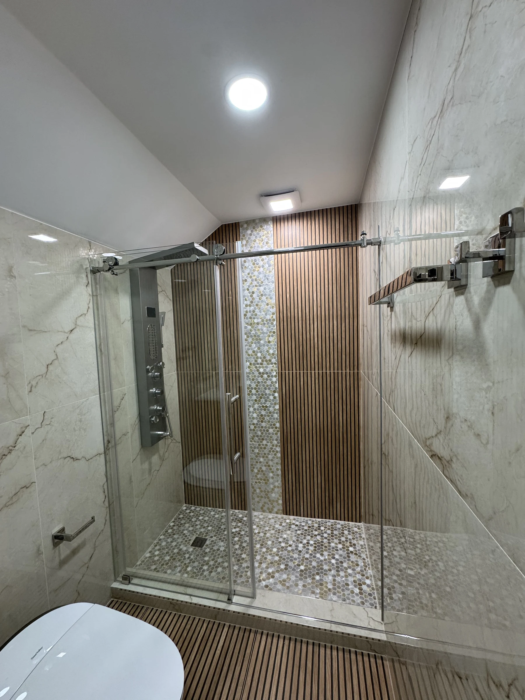 Walk-in shower with a wood-look accent wall and pebble floor