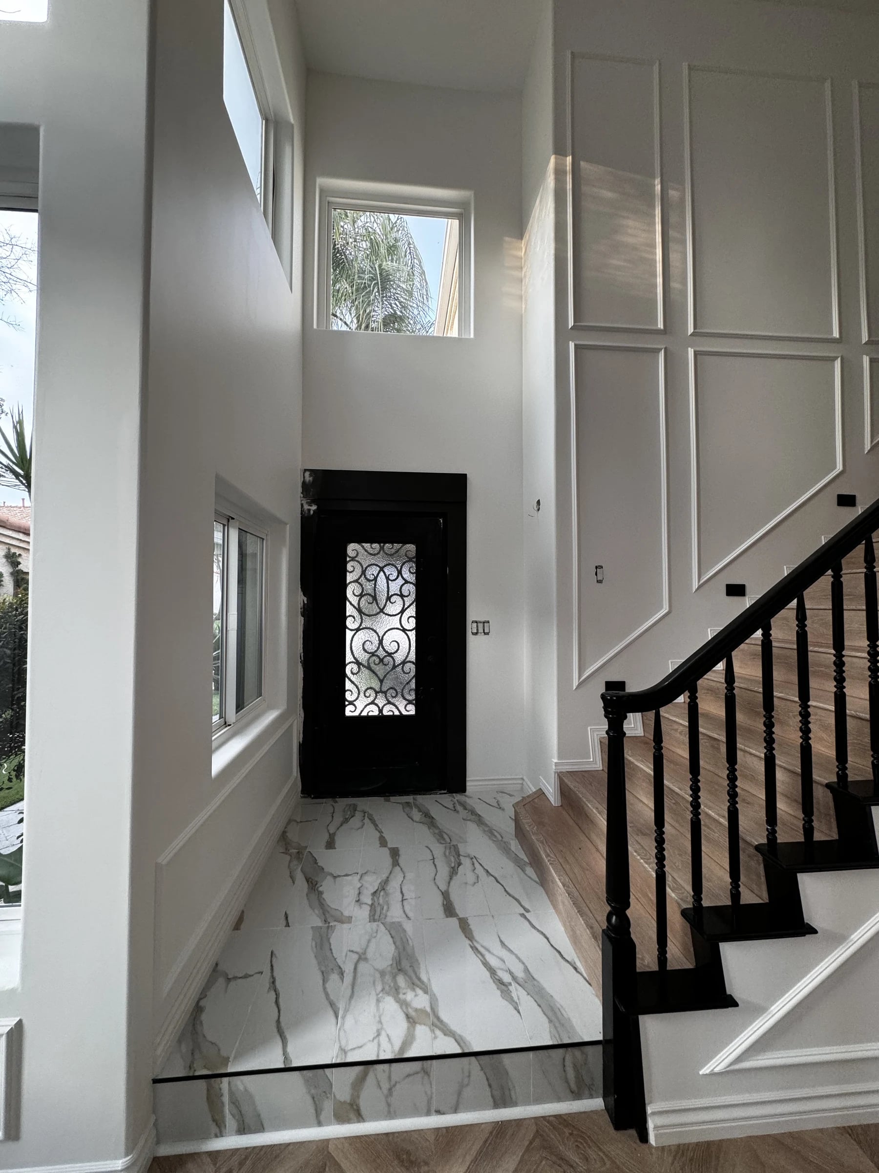 Entry with an iron door, marble-look floor and black stair rail in Pasadena