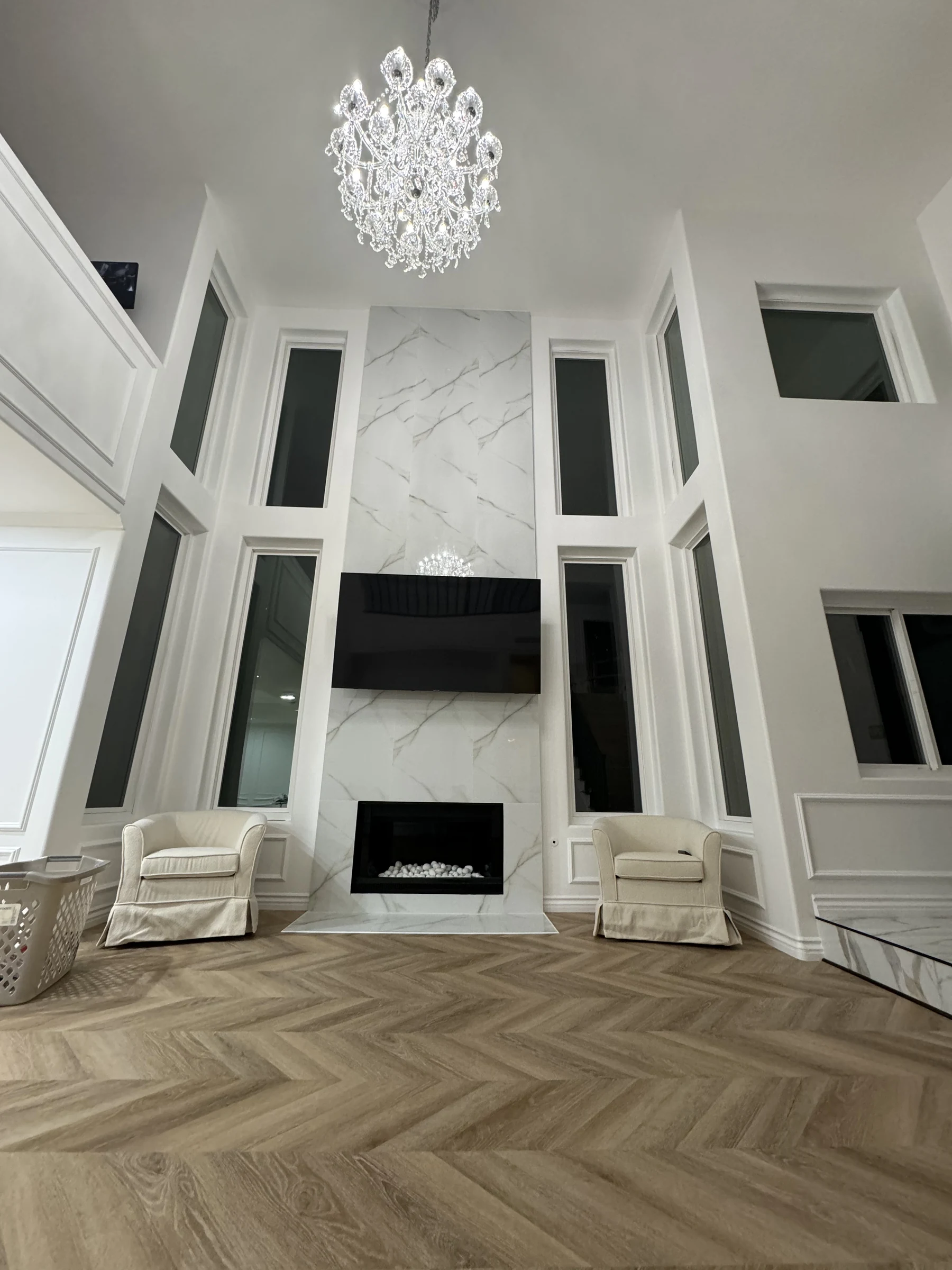 Great room with a chandelier, marble fireplace wall and tall windows in Pasadena